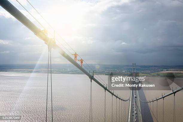 bridge workers walking on cable of suspension bridge under bright sunlight. the humber bridge, uk was built in 1981 and at the time was the worlds largest single-span suspension bridge - humber bridge stock pictures, royalty-free photos & images