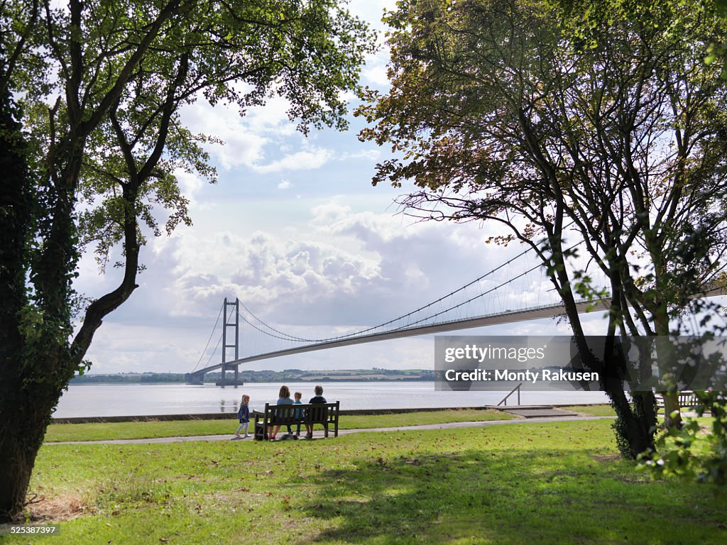 Family sitting together on bench looking at suspension bridge. The Humber Bridge, UK was built in 1981 and at the time was the worlds largest single-span suspension bridge
