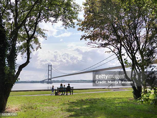 family sitting together on bench looking at suspension bridge. the humber bridge, uk was built in 1981 and at the time was the worlds largest single-span suspension bridge - hull uk stock pictures, royalty-free photos & images