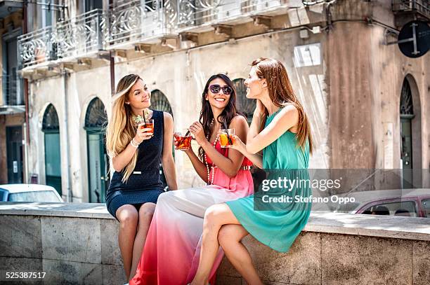 three young fashionable female friends having cocktails on sidewalk cafe wall, cagliari, sardinia, italy - glamorous woman stock-fotos und bilder