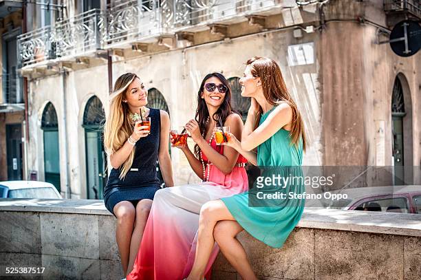 three young fashionable female friends having cocktails on sidewalk cafe wall, cagliari, sardinia, italy - glitz and glam holiday event stock pictures, royalty-free photos & images