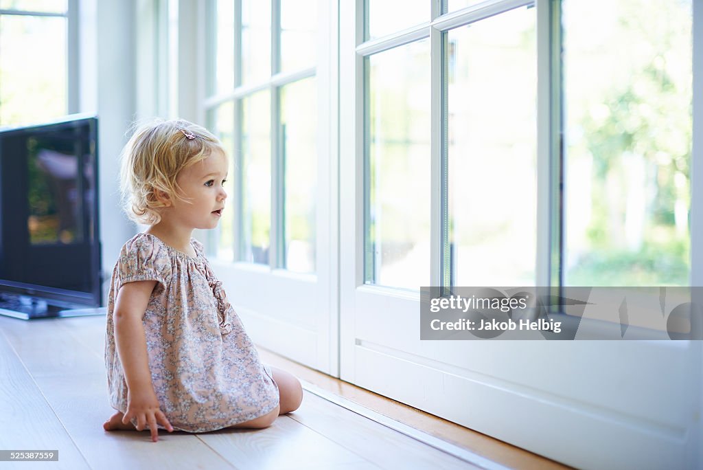 Portrait female toddler sitting on floor looking out of patio doors