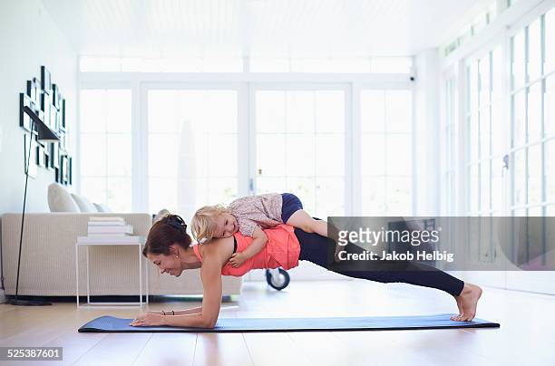 mid adult mother practicing yoga with toddler daughter on top of her - family exercising stock-fotos und bilder