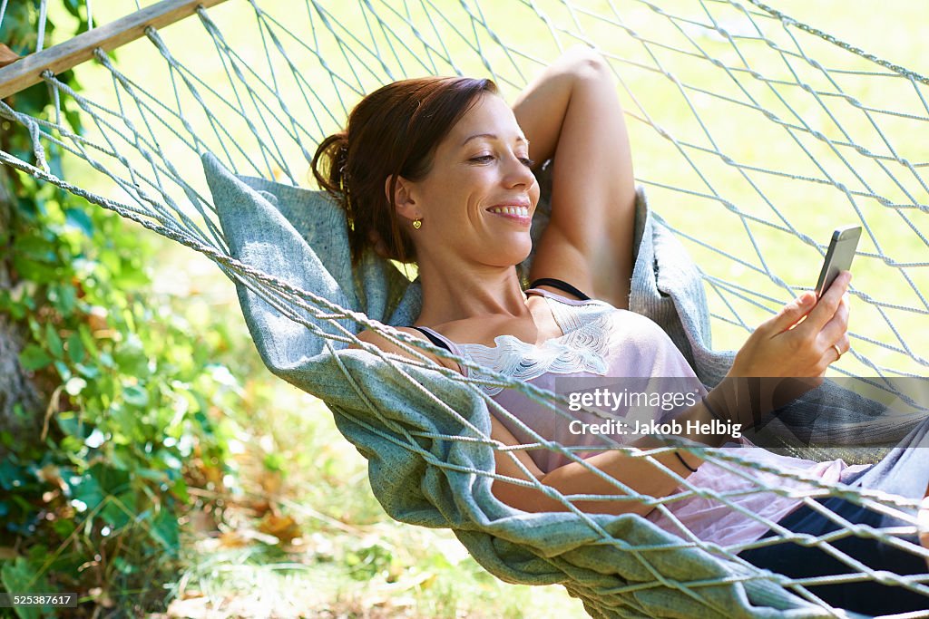 Mid adult woman reclining in garden hammock looking at smartphone