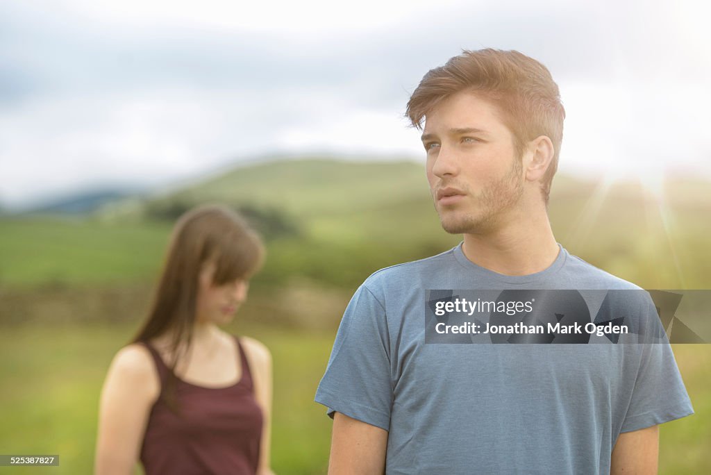 Young couple standing apart and looking away in rural landscape under bright sunny sky