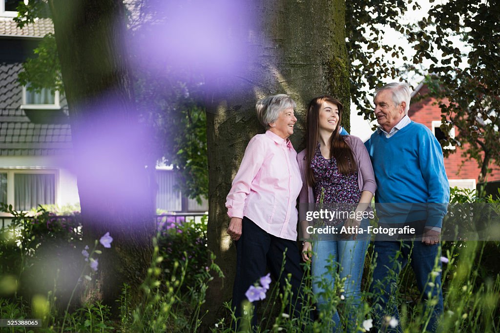 Grandparents and granddaughter standing by tree