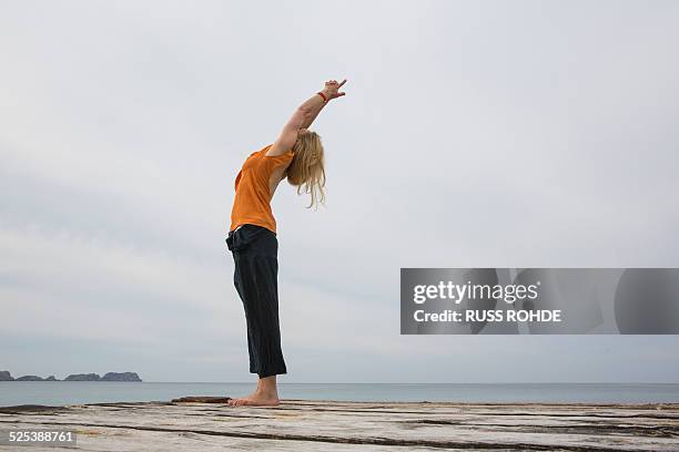 mid adult woman stretching back practicing yoga on wooden sea pier - blonde yoga stock pictures, royalty-free photos & images