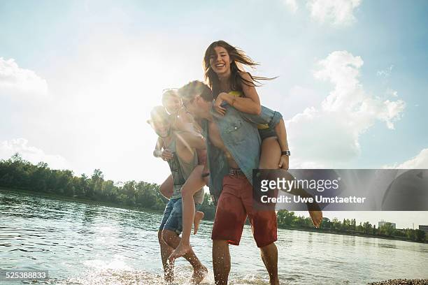 young men giving young women piggy backs - lake stock-fotos und bilder