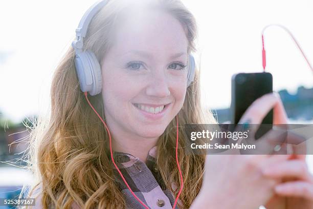 close up portrait of young woman listening to music on headphones on street - sean malyon stock-fotos und bilder