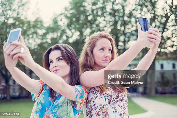 two young female friends taking selfie on smartphones side by side - sean malyon stock-fotos und bilder