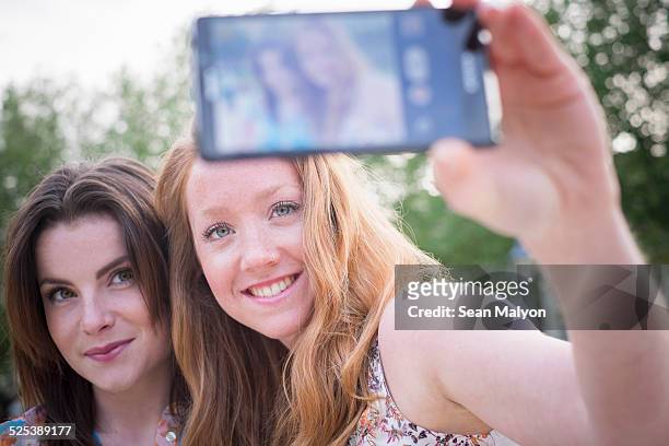 close up of two young female friends in park taking selfie on smartphone - sean malyon stock-fotos und bilder