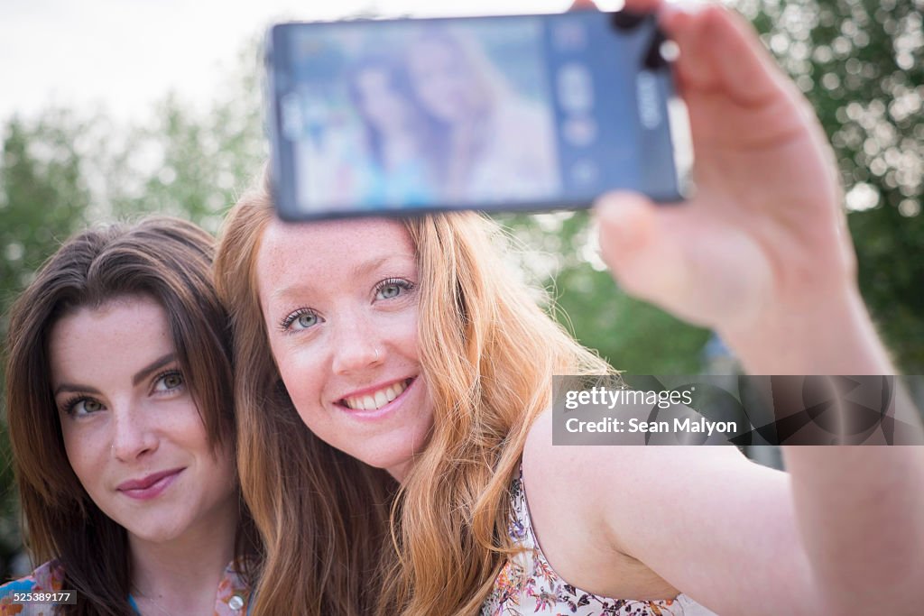 Close up of two young female friends in park taking selfie on smartphone