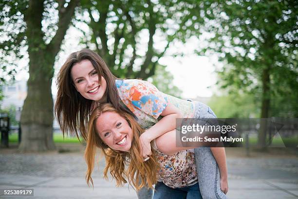 portrait of two young female best friends giving piggy back in park - sean malyon stock-fotos und bilder