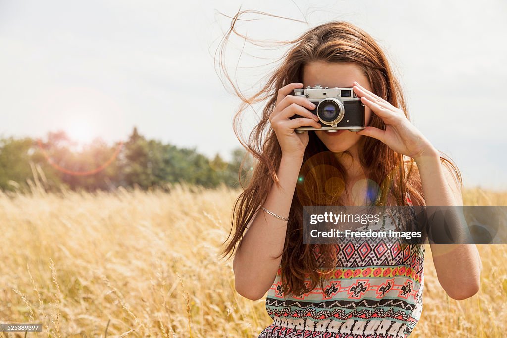 Young woman taking photo with vintage camera in field