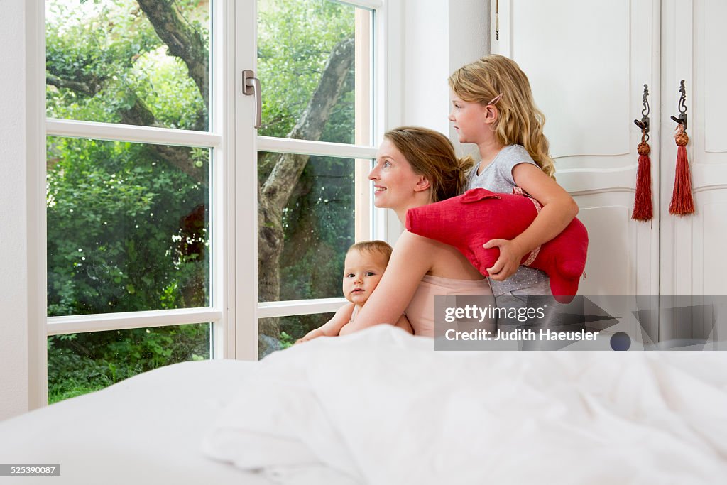 Mother and two daughters looking out of window