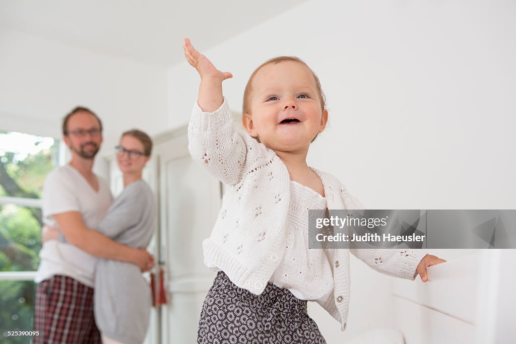 Baby with hand raised, parents in background