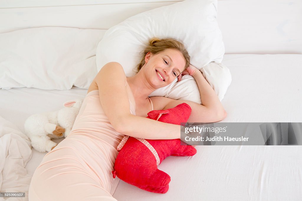 Mid adult woman lying on bed holding soft toy