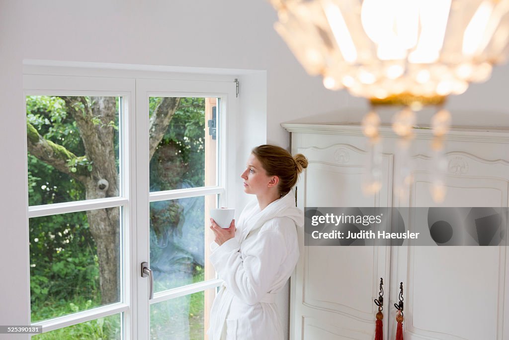 Mid adult woman wearing bathrobe looking out of window