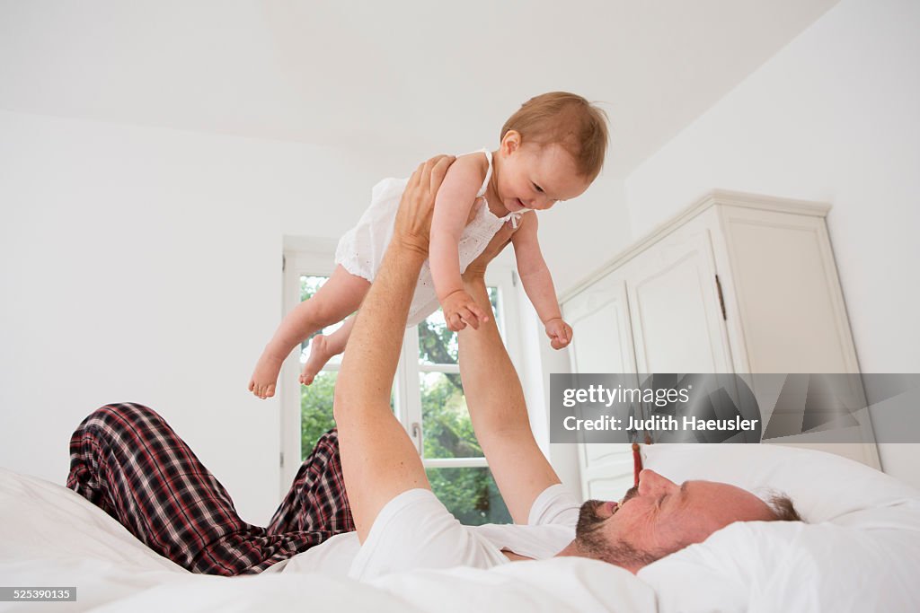 Father playing with baby daughter on bed