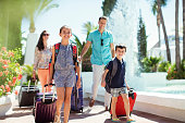 Family with suitcases passing by fountain in tourist resort