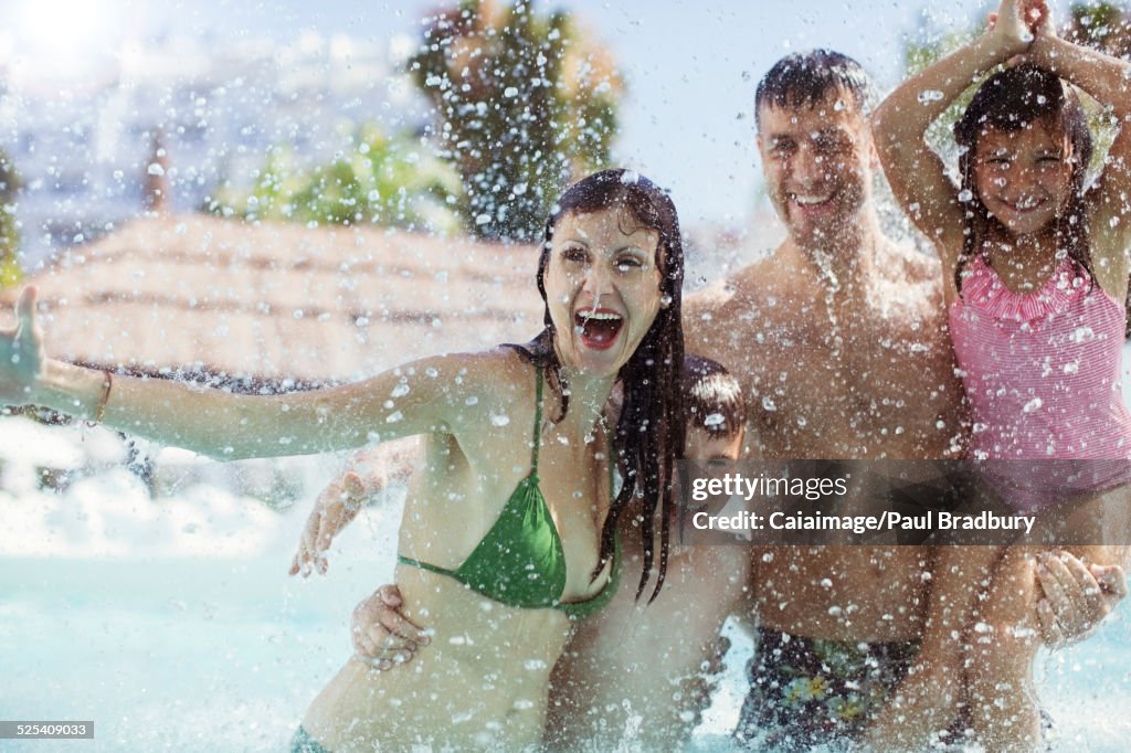 Familia con dos niños chapoteando agua y riendo en la piscina