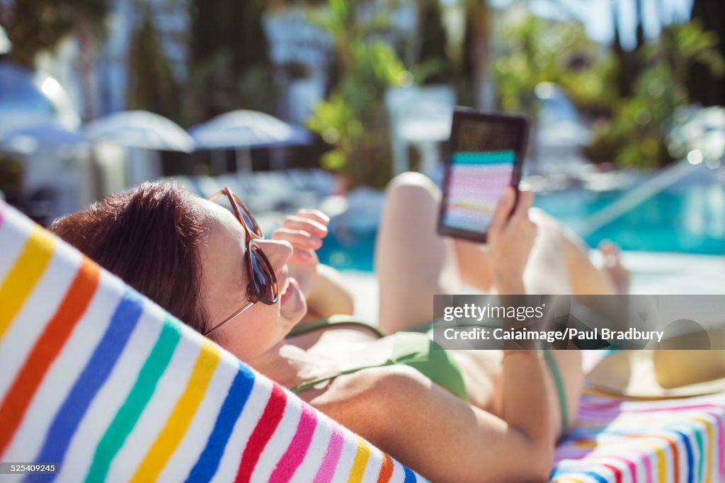 Smiling woman with digital tablet sunbathing by swimming pool