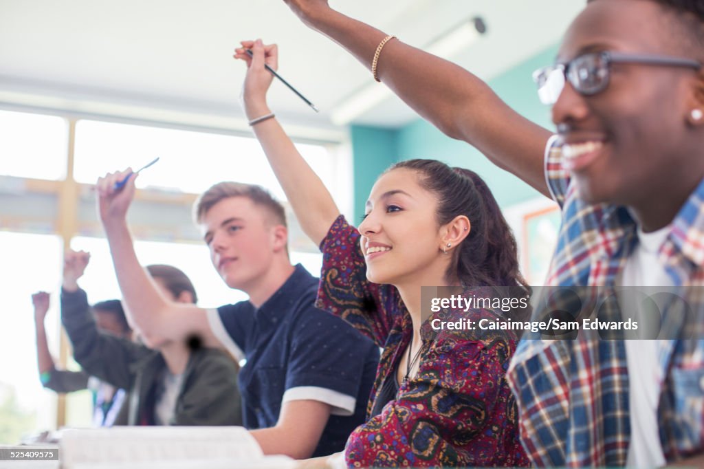 Students sitting in classroom during lesson, smiling and raising hands