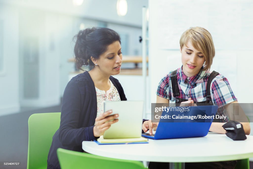 Teacher and student sitting together with digital tablet and laptop