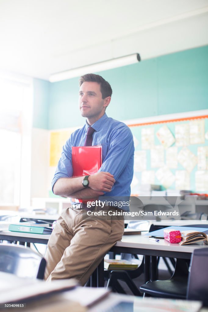 Portrait of male teacher leaning at desk in classroom