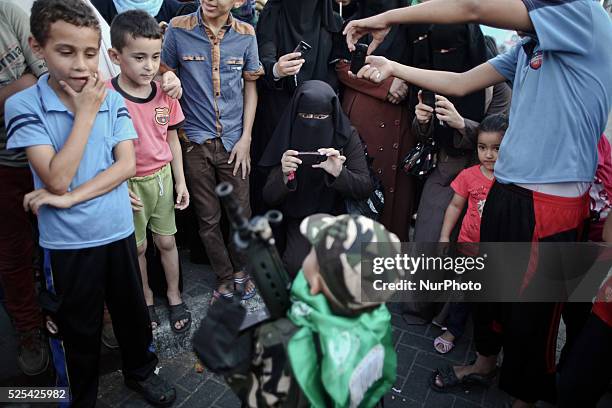 Palestinian boy holds weapon for a member of the Ezz Al-Din Al Qassam brigade, the military wing of Hamas, during a march along the streets of Gaza...