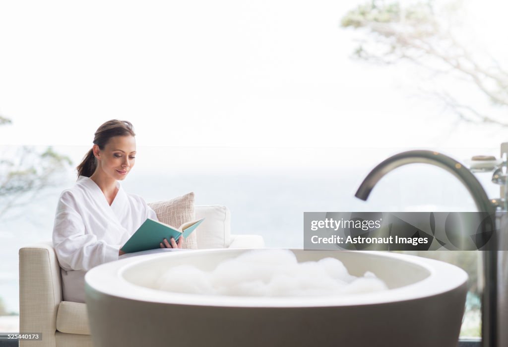 Smiling woman in bathrobe reading book in bathroom