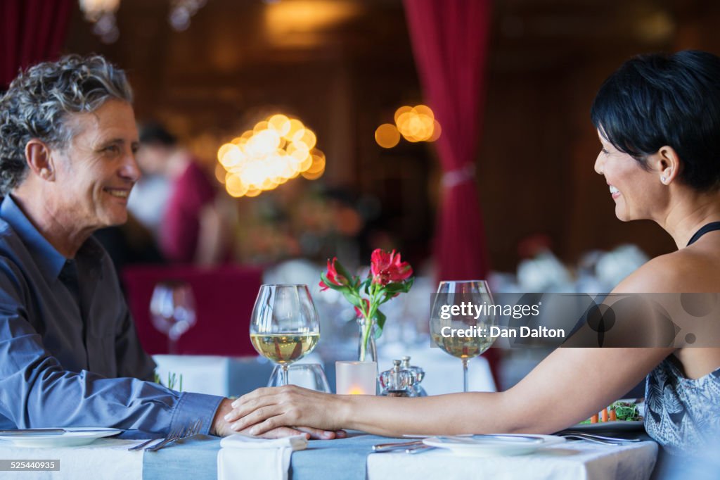 Mature couple sitting face to face and holding hands at restaurant table
