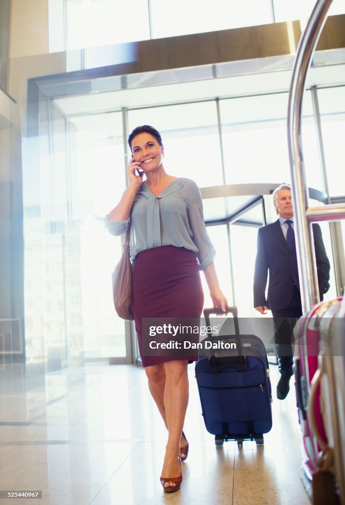 Business woman pulling suitcase and using mobile phone in lobby