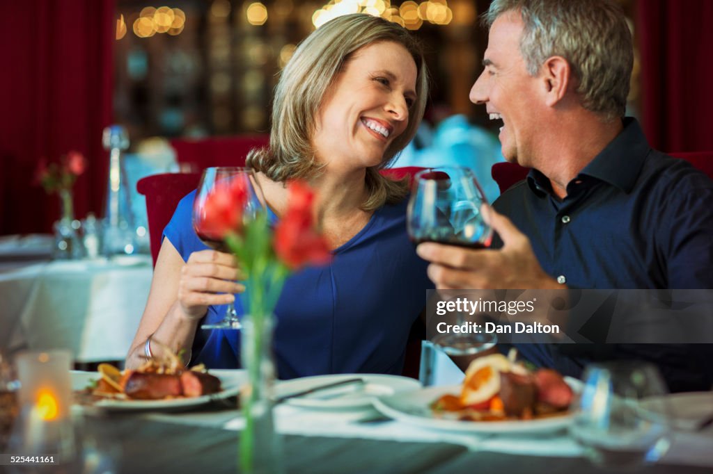 Smiling happy mature couple looking at each other and holding glasses with red wine in restaurant