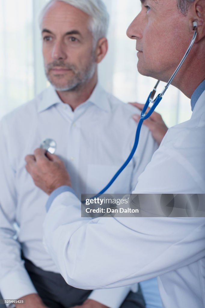 Doctor examining patient with stethoscope in office