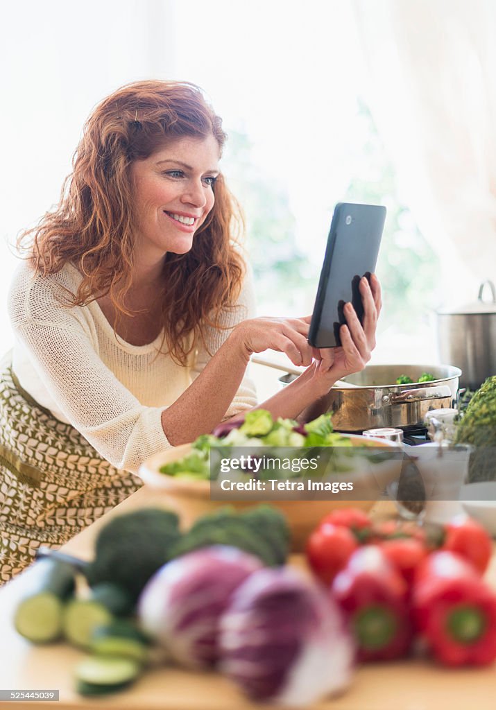 USA, New Jersey, Jersey City, Woman cooking and using digital tablet in kitchen