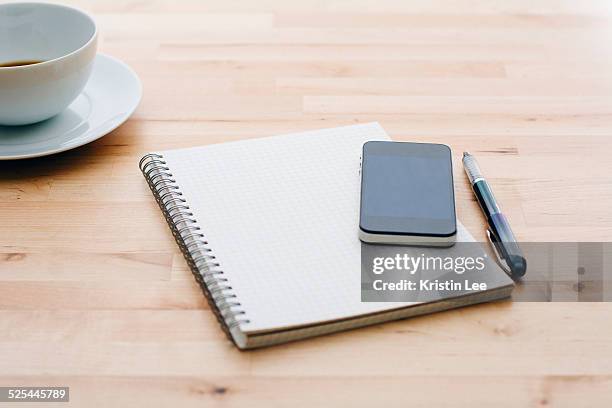 spiral notebook, ballpoint pen, mobile phone and coffee cup on wooden table - spiral notebook table stock pictures, royalty-free photos & images