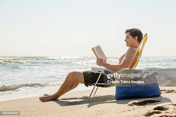 usa, florida, palm beach, side view of man sitting on deckchair and reading book - beach seat stock pictures, royalty-free photos & images