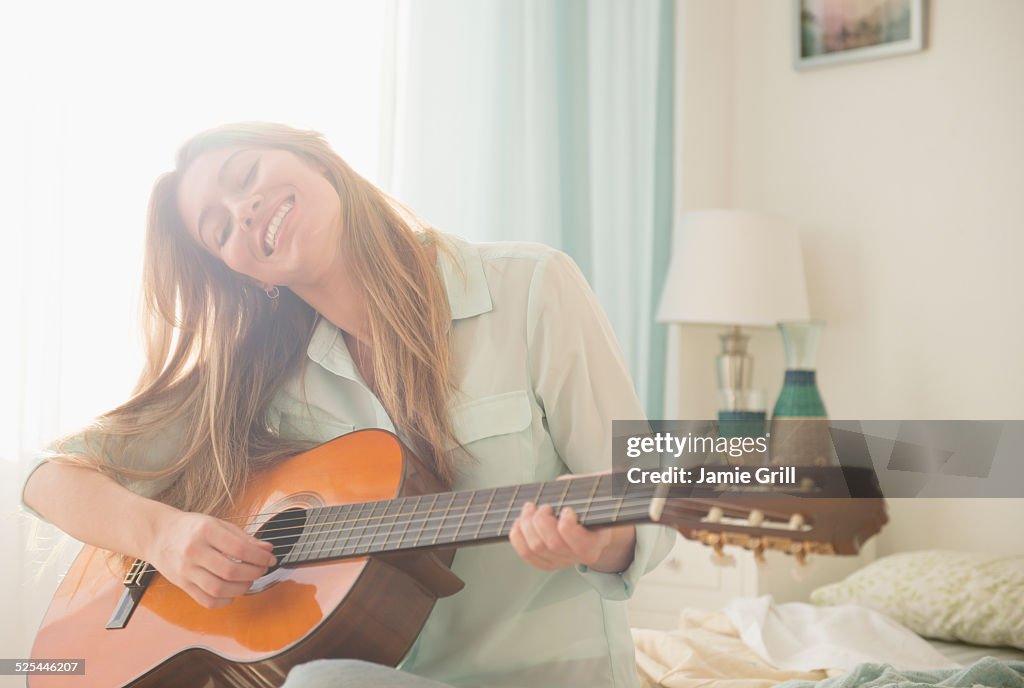 USA, New Jersey, Jersey City, Young woman playing acustic guitar on bed