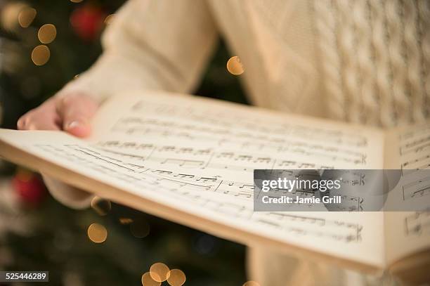 studio shot of woman holding sheet music at christmas - christmas carols stock-fotos und bilder