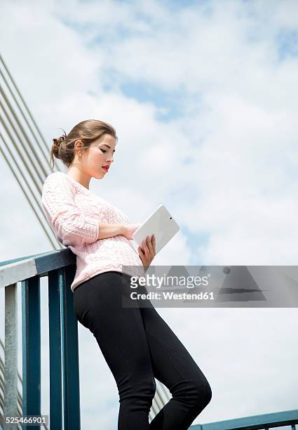 young woman leaning on railing using digital tablet - geländer stock-fotos und bilder
