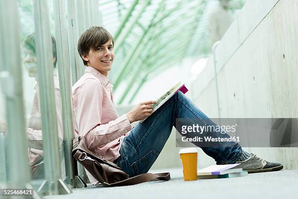 student in a university library sitting on floor reading book - sfogliare libro foto e immagini stock