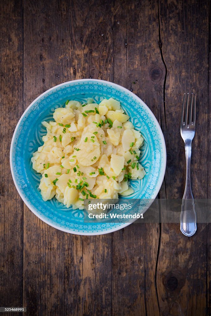 Bowl of Swabian potato salad and fork on dark wood, elevated view