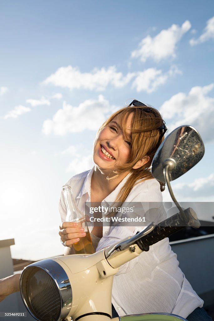 Happy teenage girl with bottle at moped