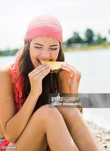 portrait of young woman eating slice of pineapple on the beach - human hair strand stock pictures, royalty-free photos & images