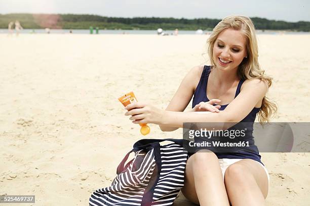 smiling young woman sitting on the beach using suncream - fore arm stock pictures, royalty-free photos & images