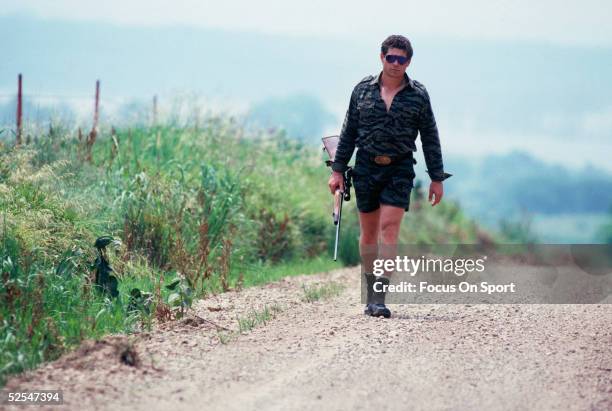 Washinton Redskins' John Riggins walks down a road with a hunting rifle.