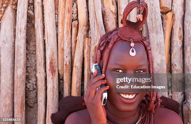 Namibia, Africa, remote nomadic Himba tribe young women with braids on modern cell phone and traditional dress in desert of Hartmann Berge in Namib...