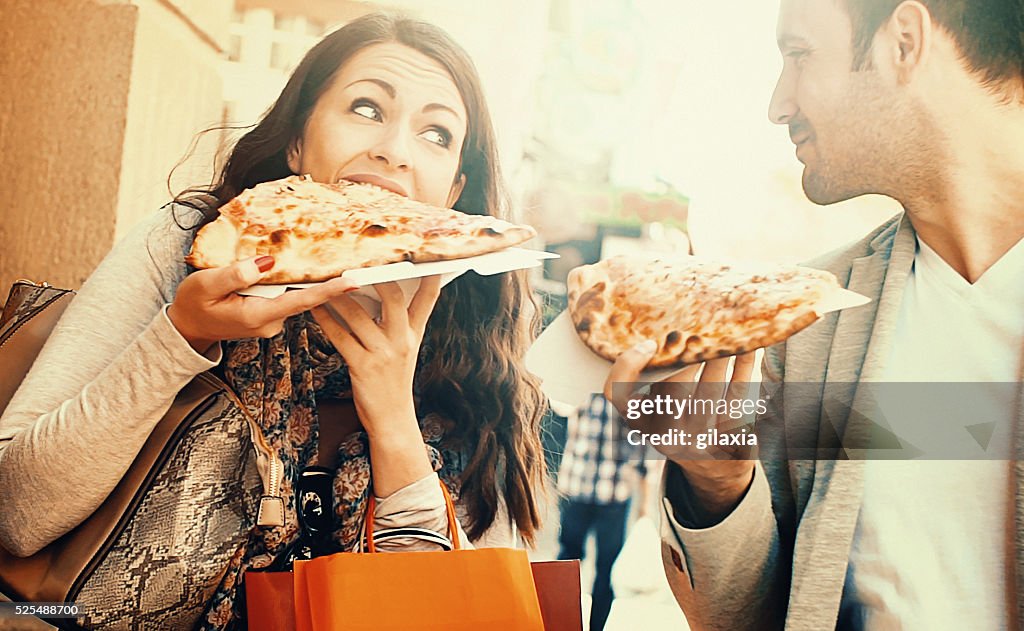 Casal comer pizza enquanto a caminhar.