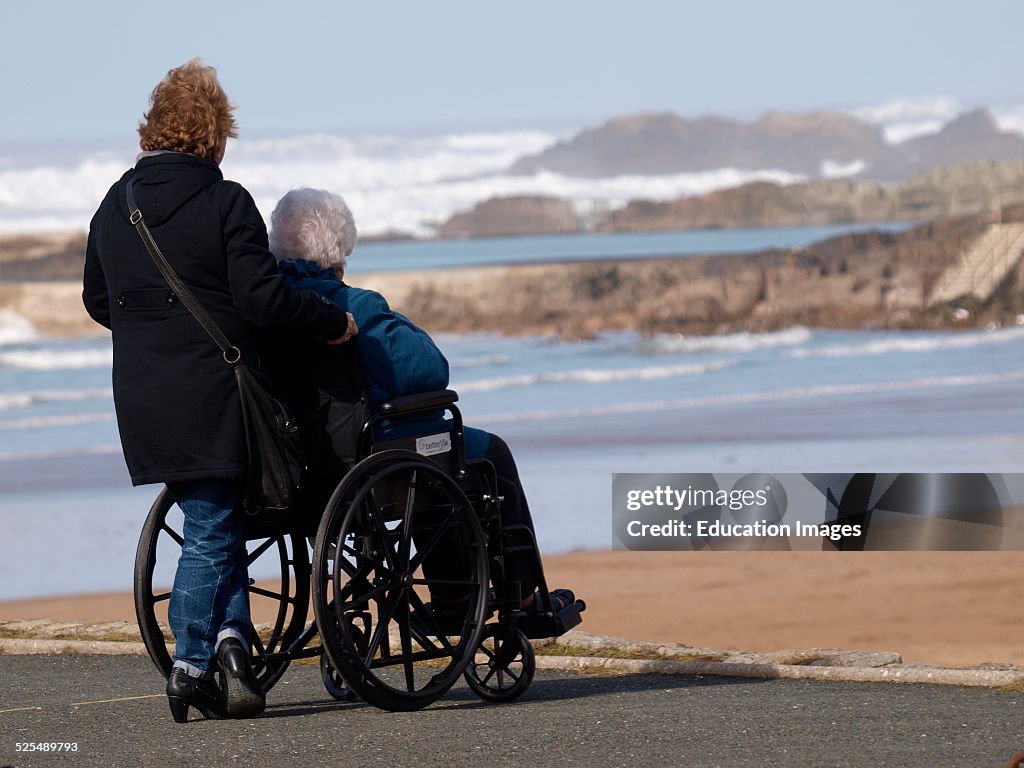 Woman in wheelchair and helper looking at the sea, Bude, Cornwall